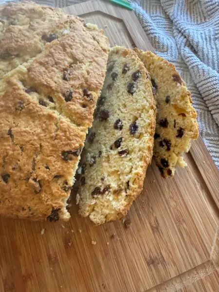 Nana's Irish Soda Bread, fresh from the oven, sitting on a cutting board with two slices cut.