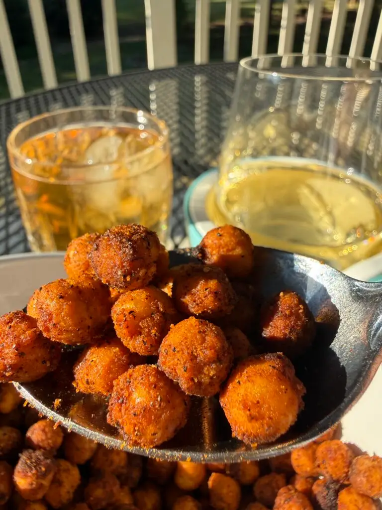 Up-close view of a spoonful of crispy roasted chickpeas, above a bowl of the same, with two cocktails behind the bowl.