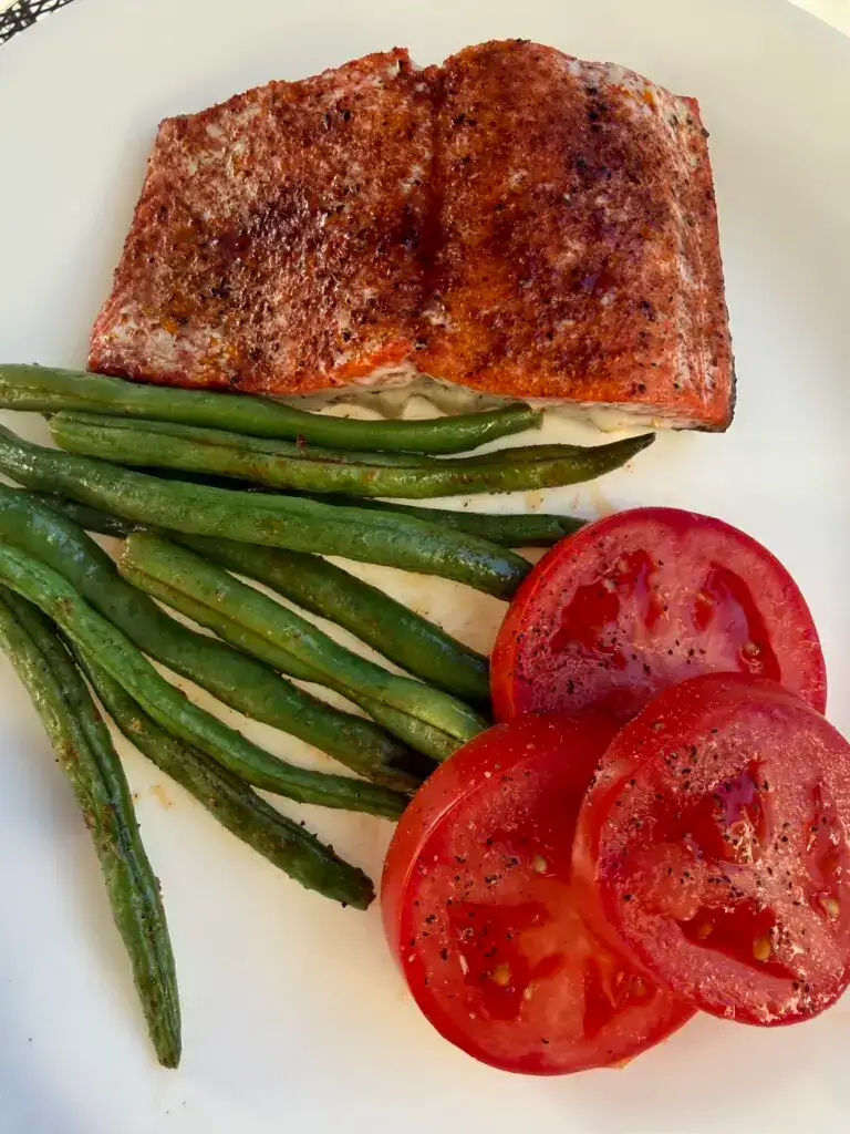 Roasted Salmon and Green Beans on a white plate alongside fresh sliced red tomatoes.