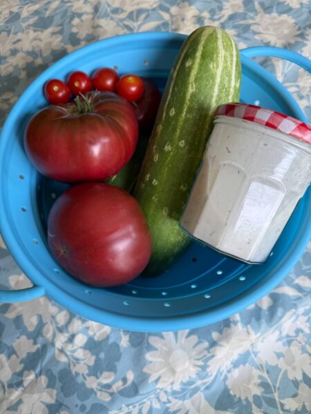 Tomatoes, Cucumber, and a mason jar of Easy German Salad Dressing in a blue colander
