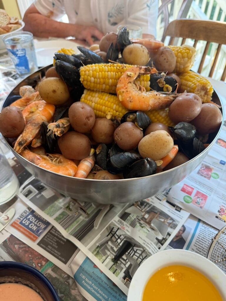 Large bowl filled with classic low country boil, consisting of corn, potatoes, shrimp, mussels, and sausage, sitting on a newspaper covered table.
