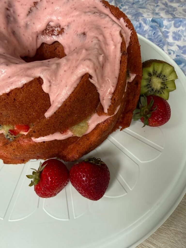 Strawberry Cake with Kiwi and Strawberry Filling, on a white platter with strawberries and half of a kiwi